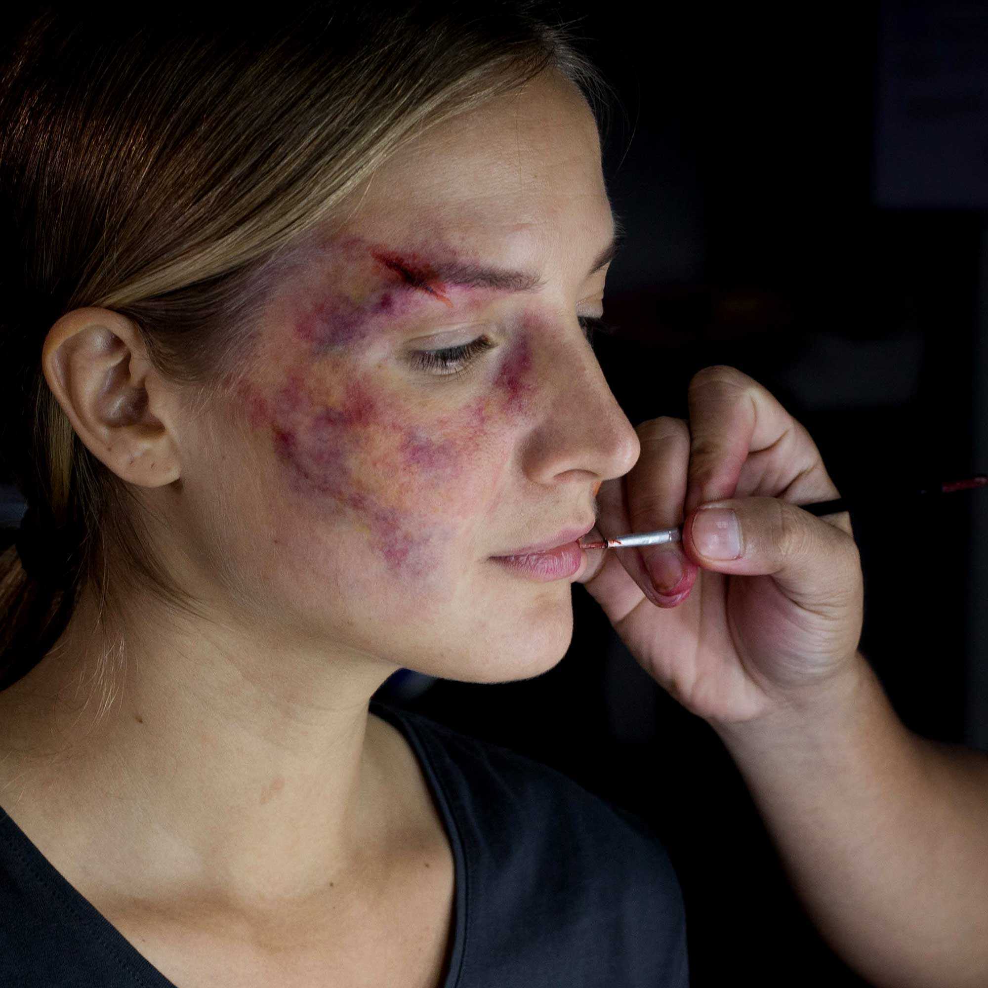 Side-profile model with bruise-style special effects makeup while a makeup artist applies detail with a brush