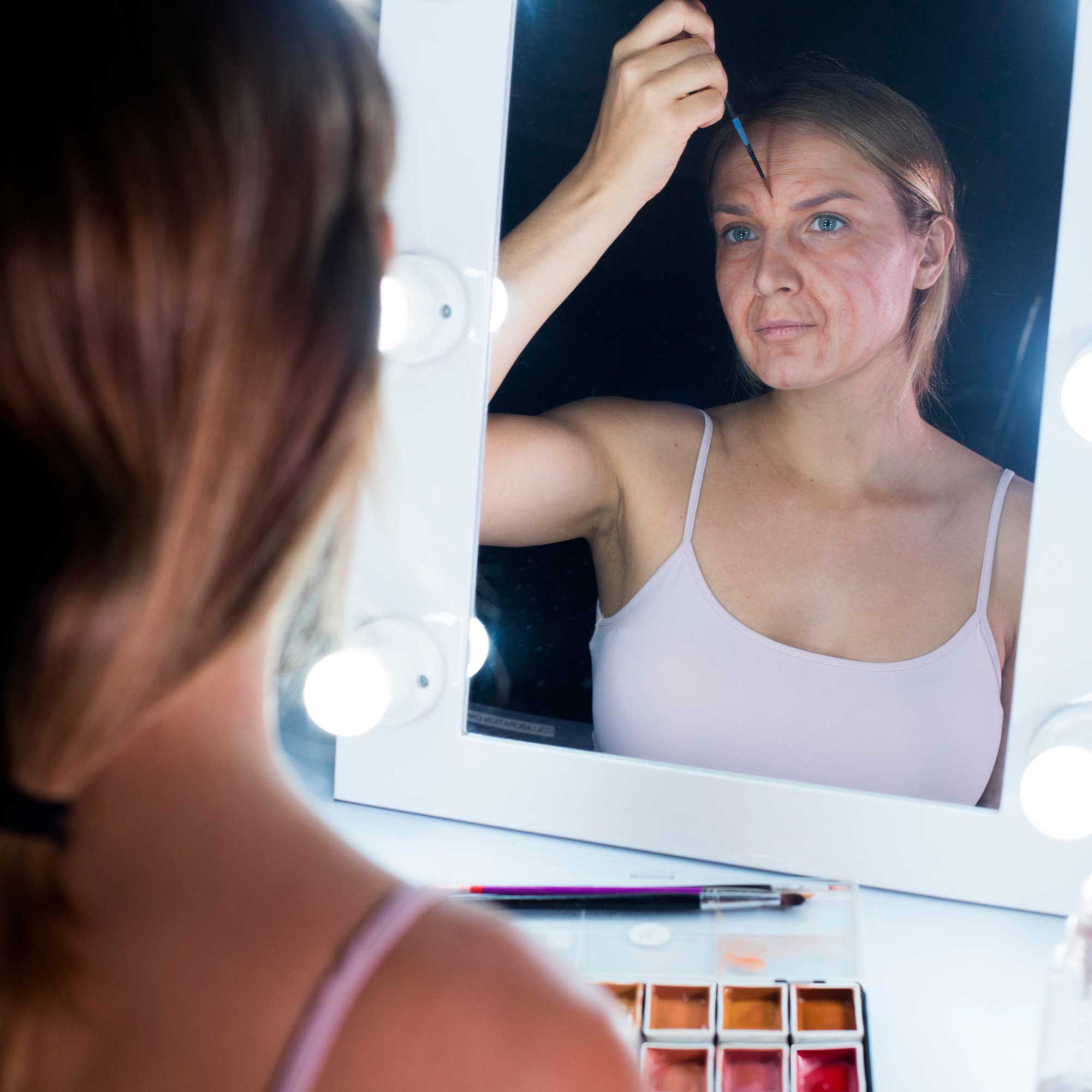 Model checking aged makeup result in mirror beside flesh tone palette