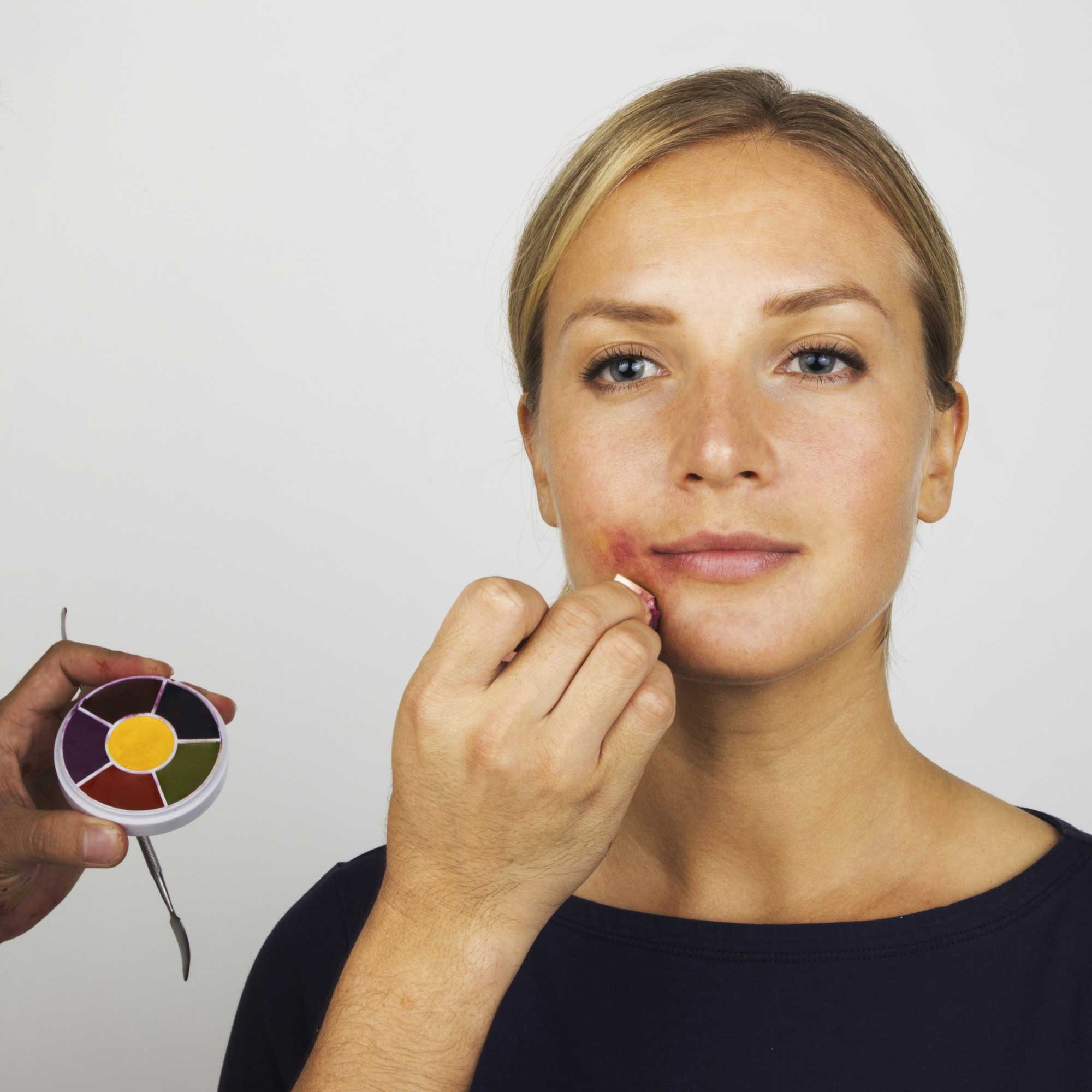 Makeup artist applying mouth-corner bruise SFX to model using 6 Color Bruise Wheel and metal applicator